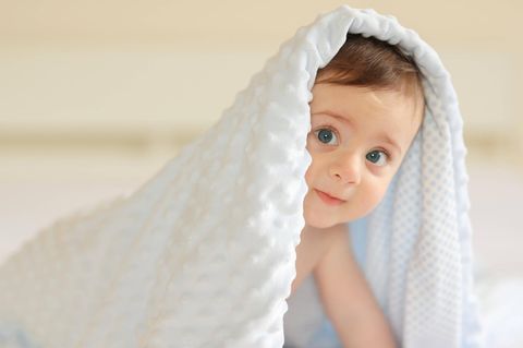 Abnehmspritzen können Kinderwunsch erfüllen: Ein Baby krabbelt unter einer weißen Decke hervor