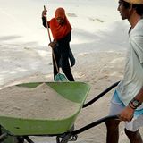 2 Menschen mit Schubkarre im Sand