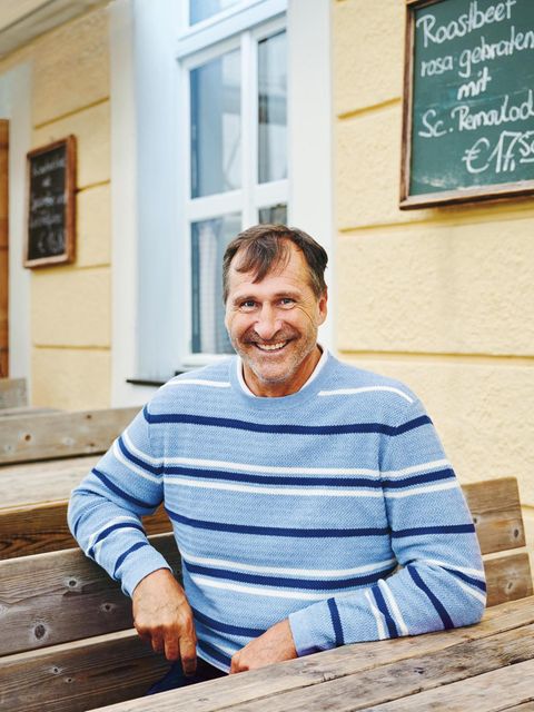 Lars Riedel im hellblauen Pullover vor einem Wirtshaus am Tegernsee