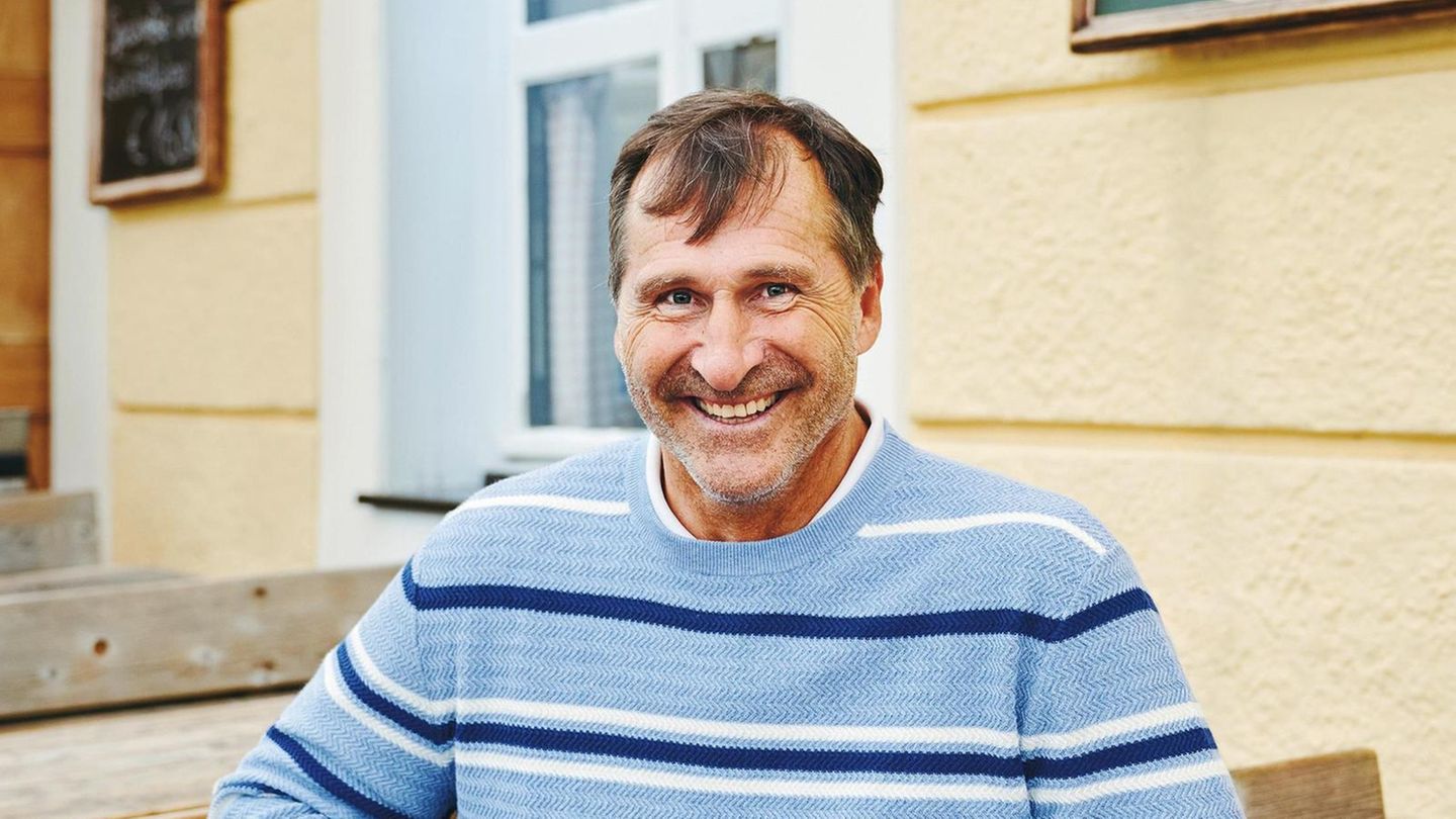 Lars Riedel im hellblauen Pullover vor einem Wirtshaus am Tegernsee