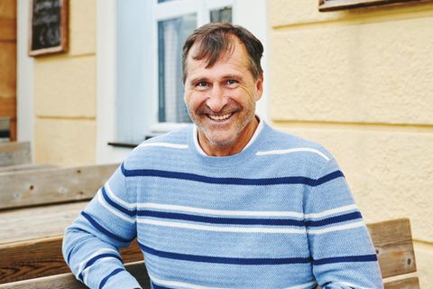 Lars Riedel im hellblauen Pullover vor einem Wirtshaus am Tegernsee