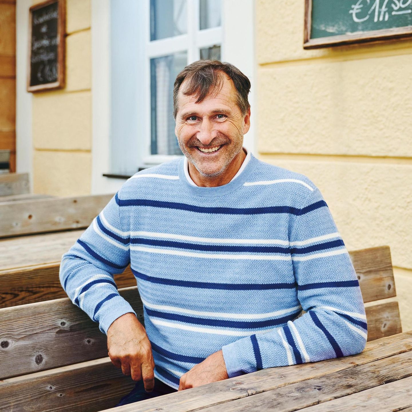 Lars Riedel im hellblauen Pullover vor einem Wirtshaus am Tegernsee