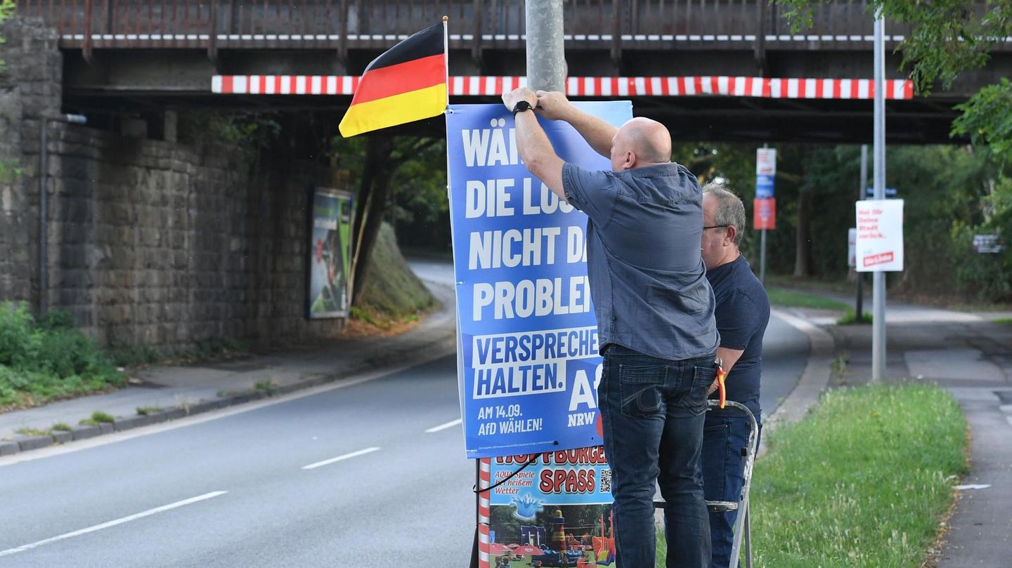 Zwei Männer bringen AfD Plakat an einer Straße an