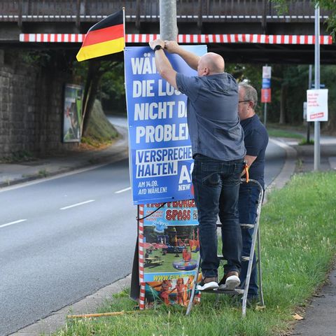 Zwei Männer bringen AfD Plakat an einer Straße an