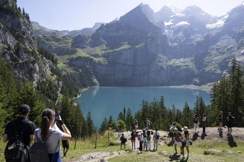 Auswanderziel: Wiese, Blauer Himmel, schneebedeckte Gipfellandschaft in der Schweiz, Wanderer vor Bergsee