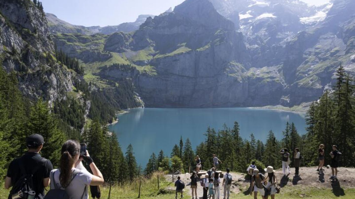 Auswanderziel: Wiese, Blauer Himmel, schneebedeckte Gipfellandschaft in der Schweiz, Wanderer vor Bergsee