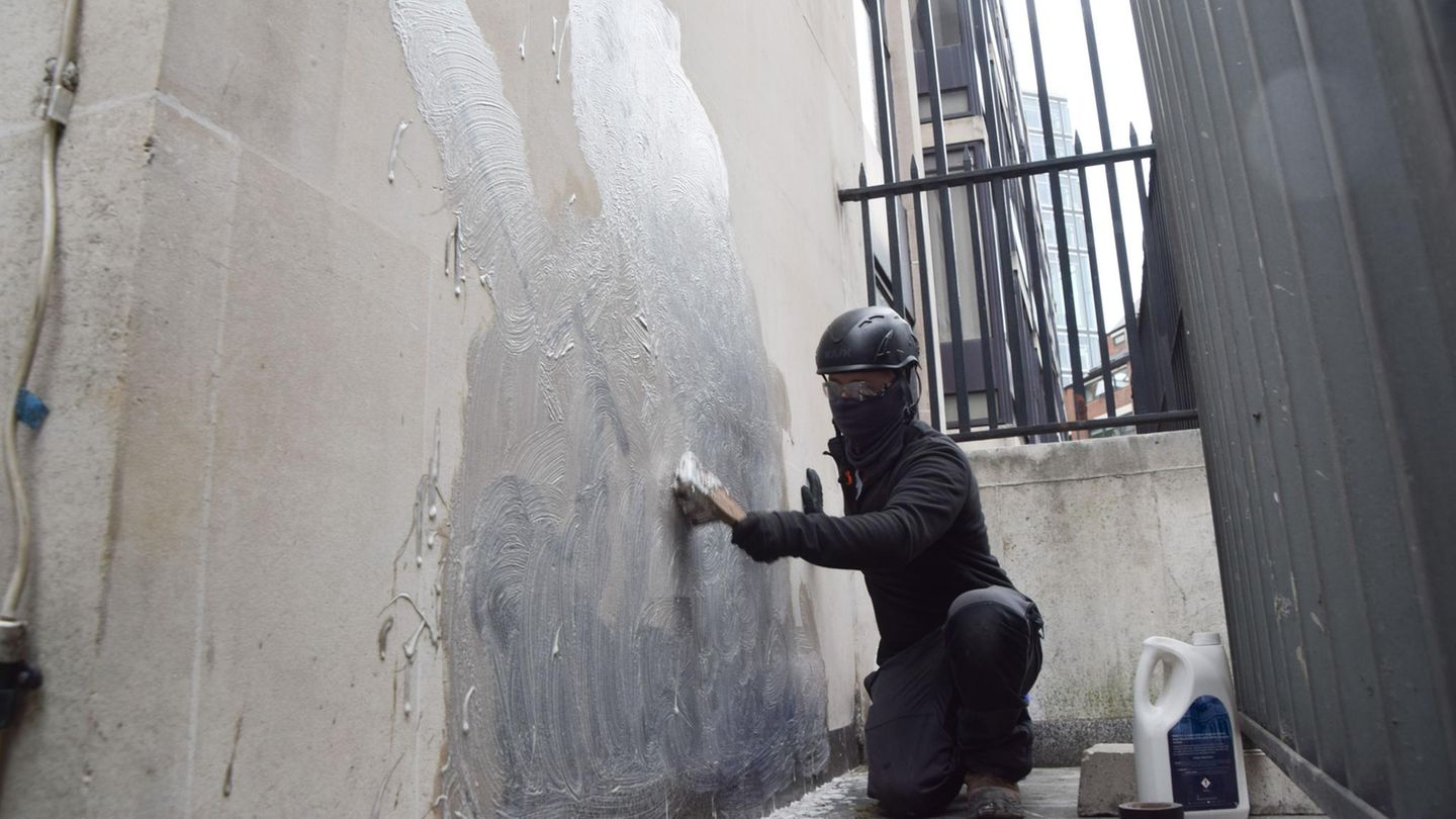 Eine Person schrubbt das neueste Kunstwerk des britischen Künstlers Banksy an den Royal Courts of Justice ab