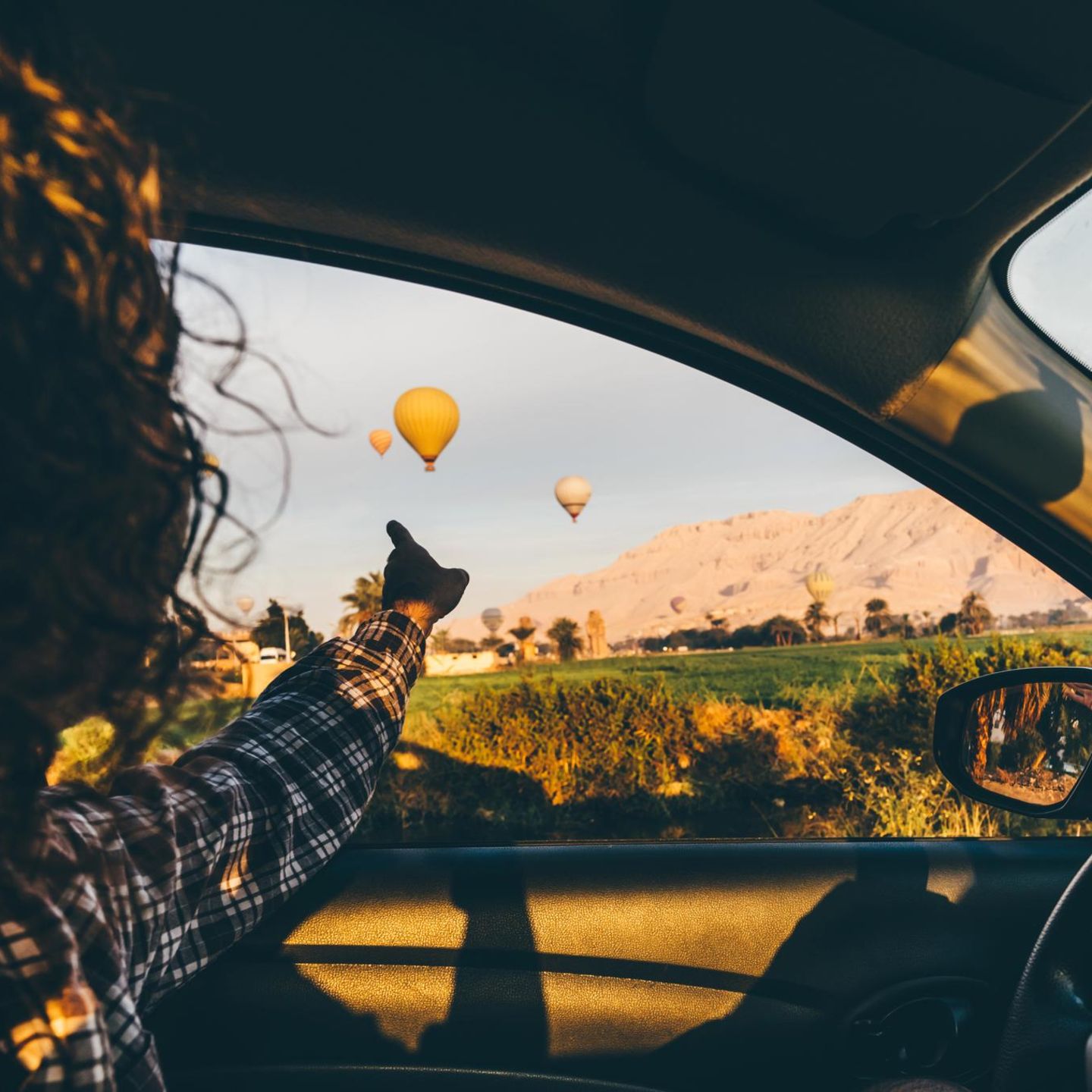 Eine Frau sitzt am Steuer und zeigt auf Heißluftballons am Himmel neben dem Auto