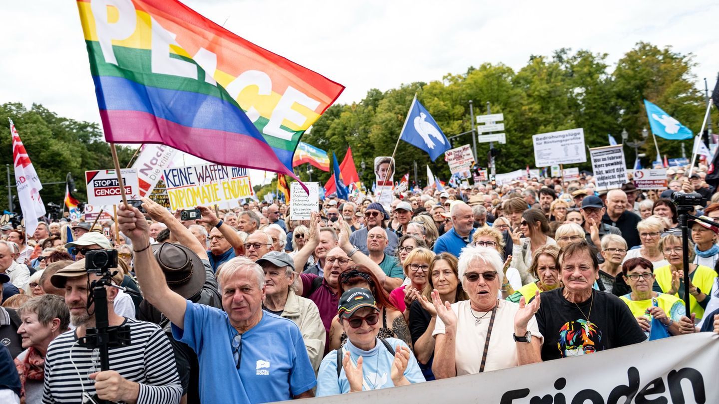 Bei der Demo in Berlin schwenken Menschen Fahnen, auf denen "Peace" steht und eine Friedenstaube abgebildet ist