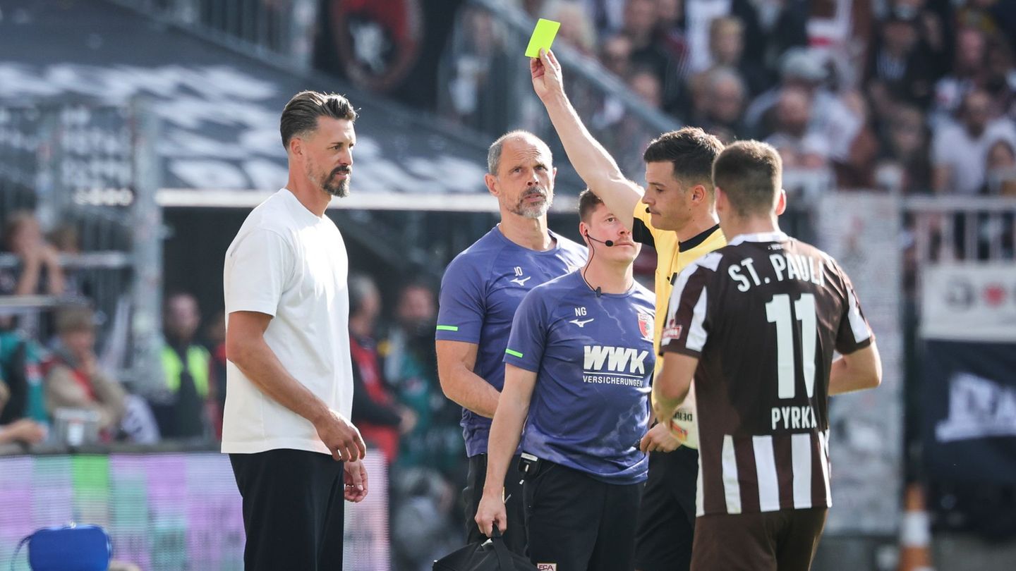 Schiedsrichter Harm Osmers zeigt Trainer Sandro Wagner (FC Augsburg, l) die gelbe Karte. Foto: Christian Charisius/dpa