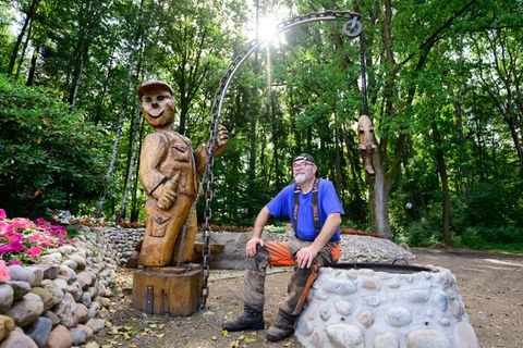 Motorsägenkünstler Andree Löbnitz neben einer Holzskulptur, die er aus einem Holzstamm schnitzte. Foto: Philipp Schulze/dpa