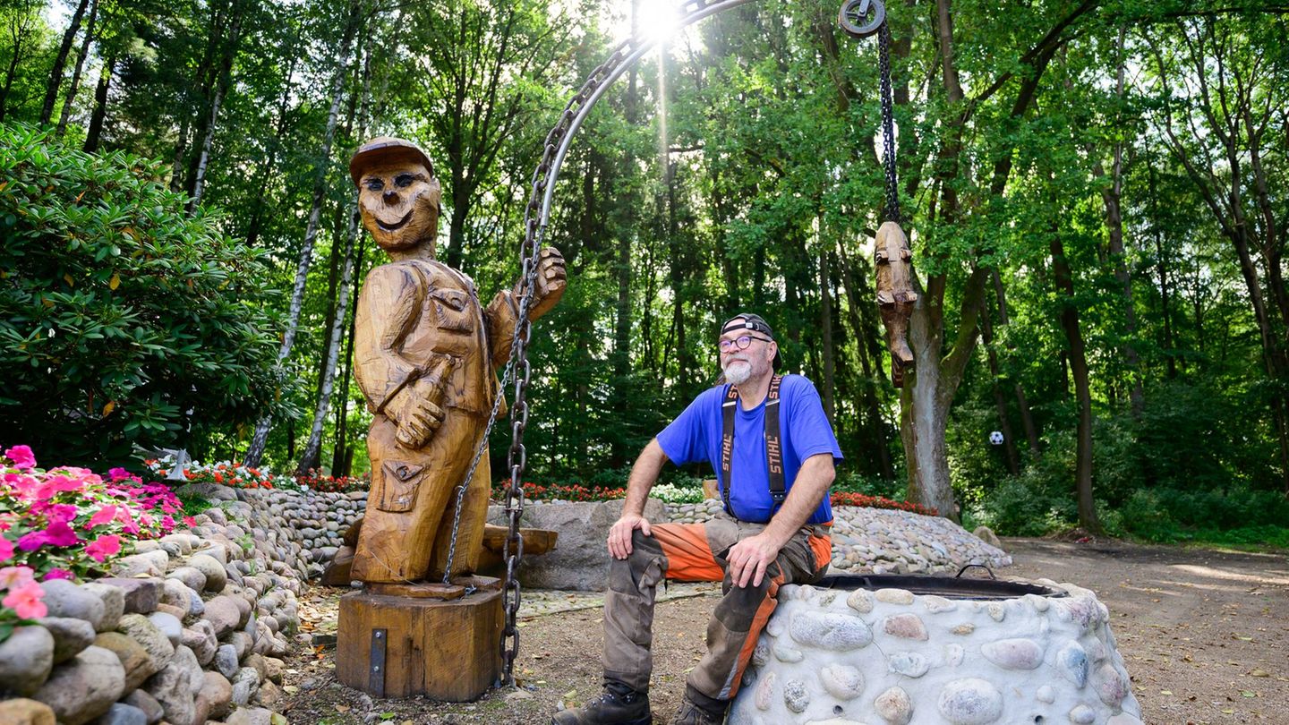 Motorsägenkünstler Andree Löbnitz neben einer Holzskulptur, die er aus einem Holzstamm schnitzte. Foto: Philipp Schulze/dpa