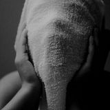 Fotografie: Ein Kind hält sich ein Handtuch vor das Gesicht und hält es mit den Händen. Der Mund ist weit offen