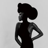 Fotografie: Eine Person trägt ein schwarzes Kleid und einen runden schwarzen Hut. Sie macht eine elegante Pose