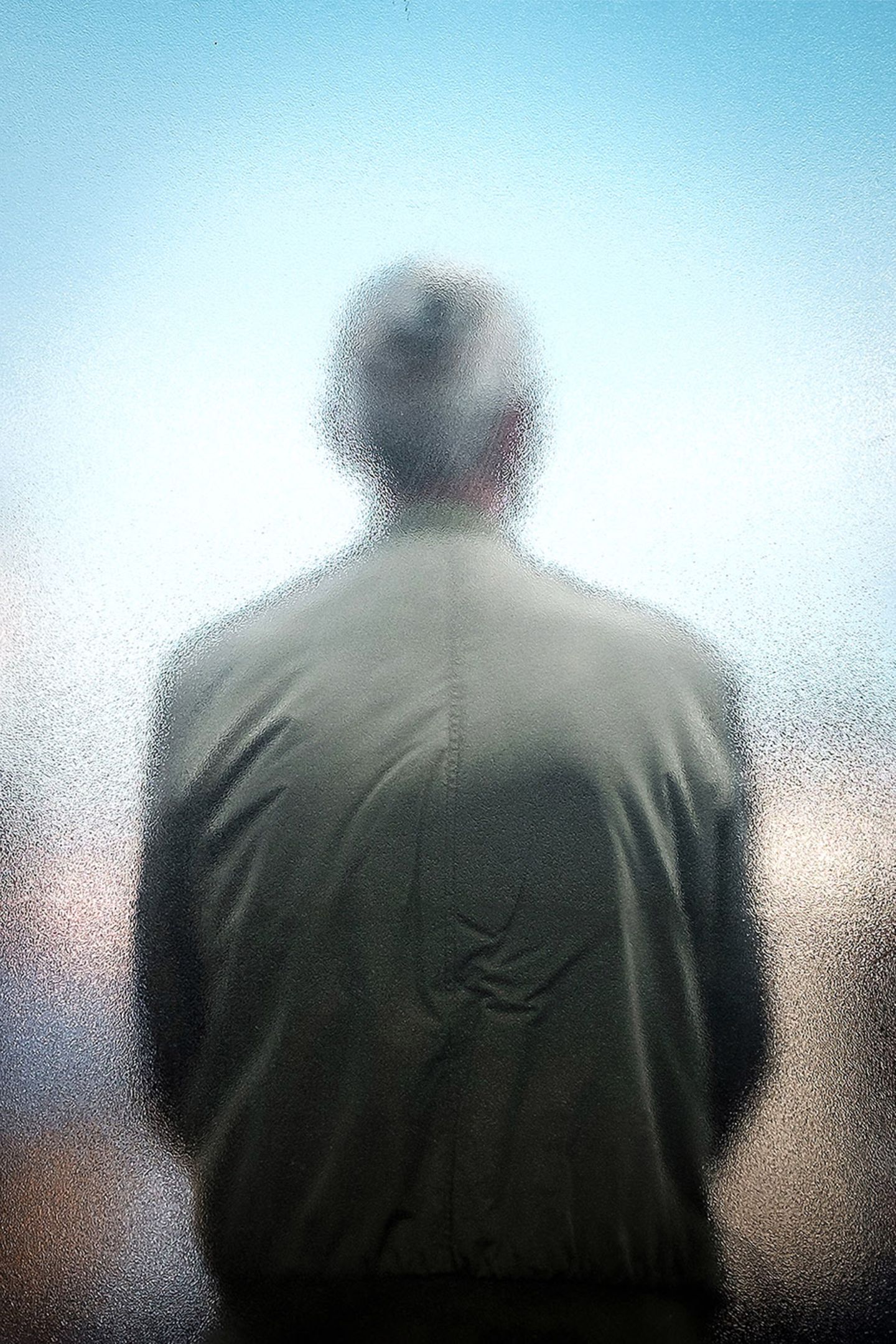 Fotografie: Eine Person von hinten, die mit dem Rücken an einer Scheibe lehnt