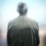 Fotografie: Eine Person von hinten, die mit dem Rücken an einer Scheibe lehnt