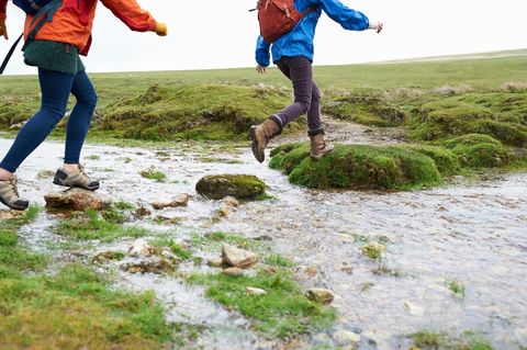 Two hikers step across the rocks in a small stream