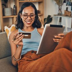 Lächelnde gemischtrassige Frau, die Kreditkarte für E-Commerce auf digitalem Tablet zu Hause verwendet.