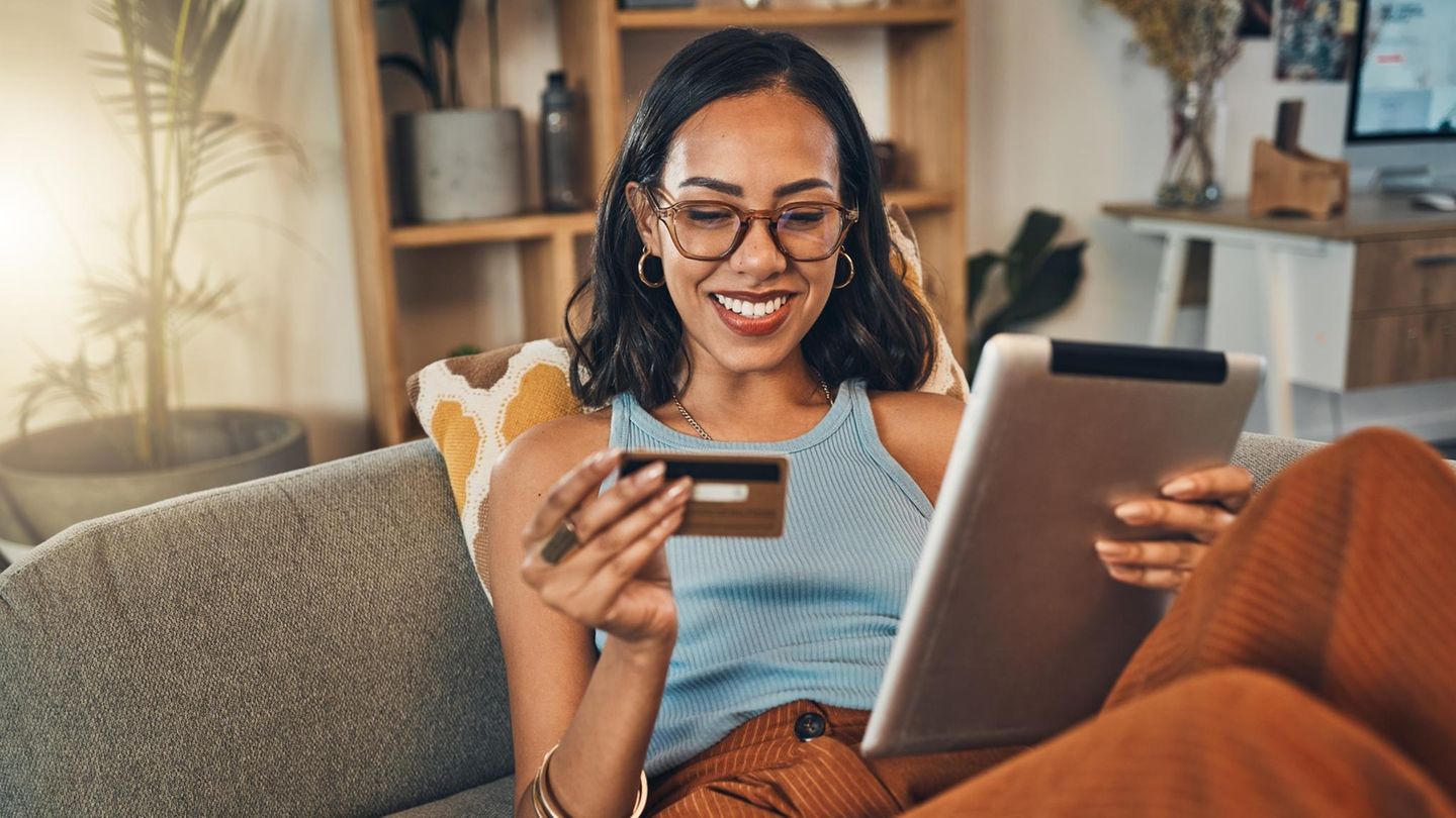 Lächelnde gemischtrassige Frau, die Kreditkarte für E-Commerce auf digitalem Tablet zu Hause verwendet.