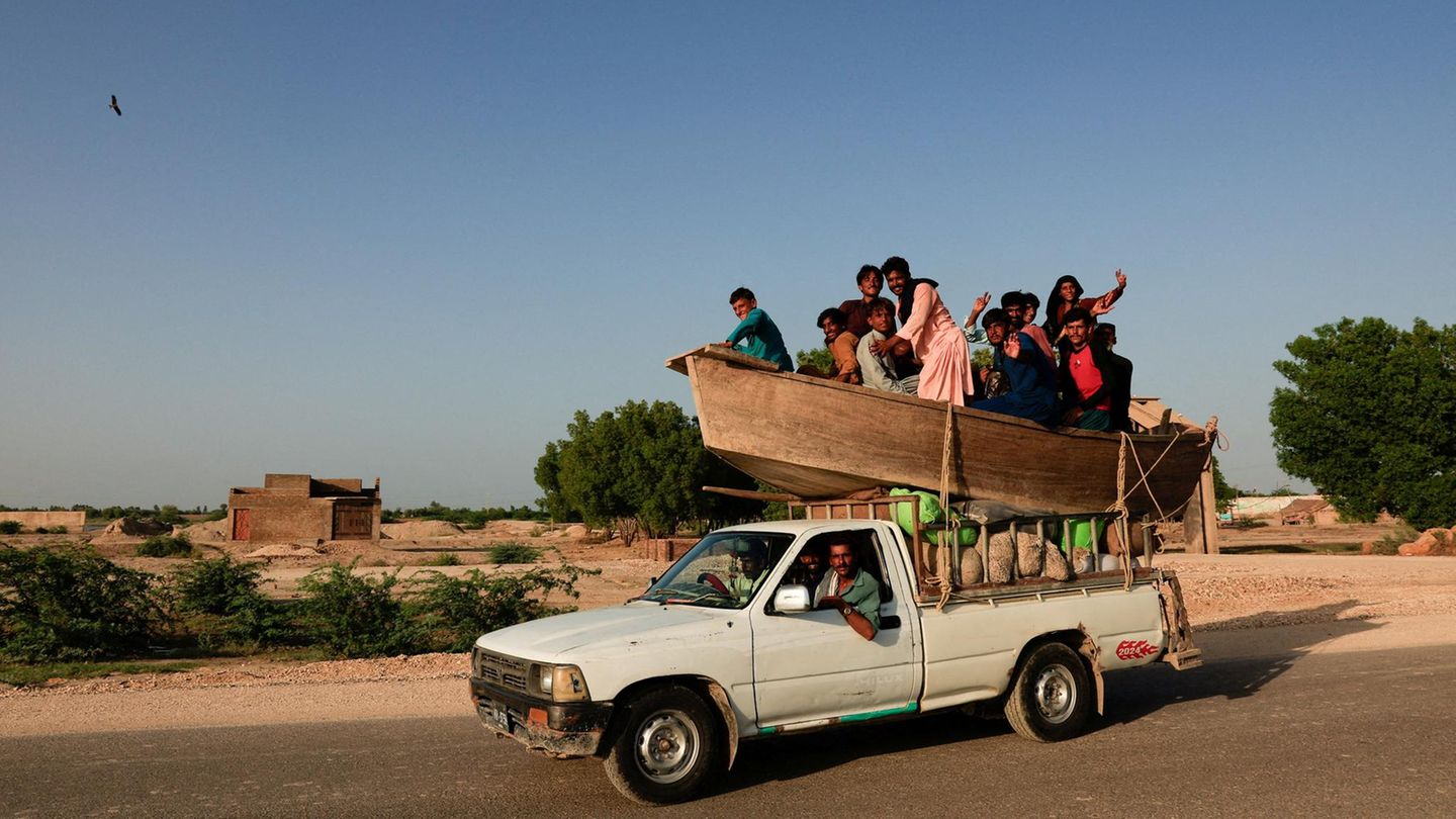 Sehwan, Pakistan. Eine Gruppe von Menschen macht sich mit einem Boot … äh, Auto …, äh, Boot-auf-Auto auf dem Weg in die vom Monsunregen überfluteten Gebiete