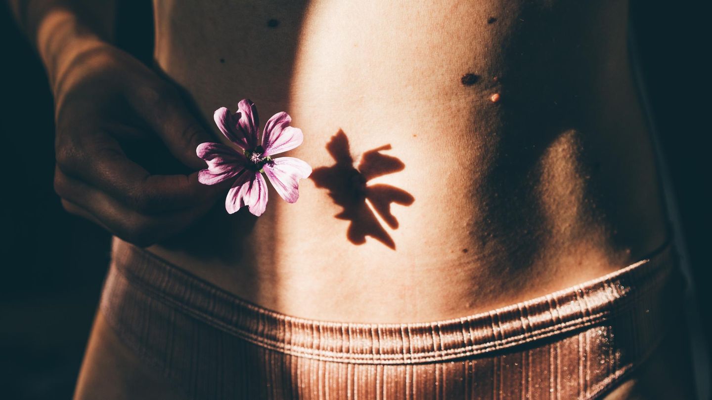 Frauengesundheit und Warnzeichen: Eine Blume vor einem weiblichen Bauch