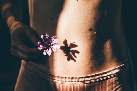 Frauengesundheit und Warnzeichen: Eine Blume vor einem weiblichen Bauch