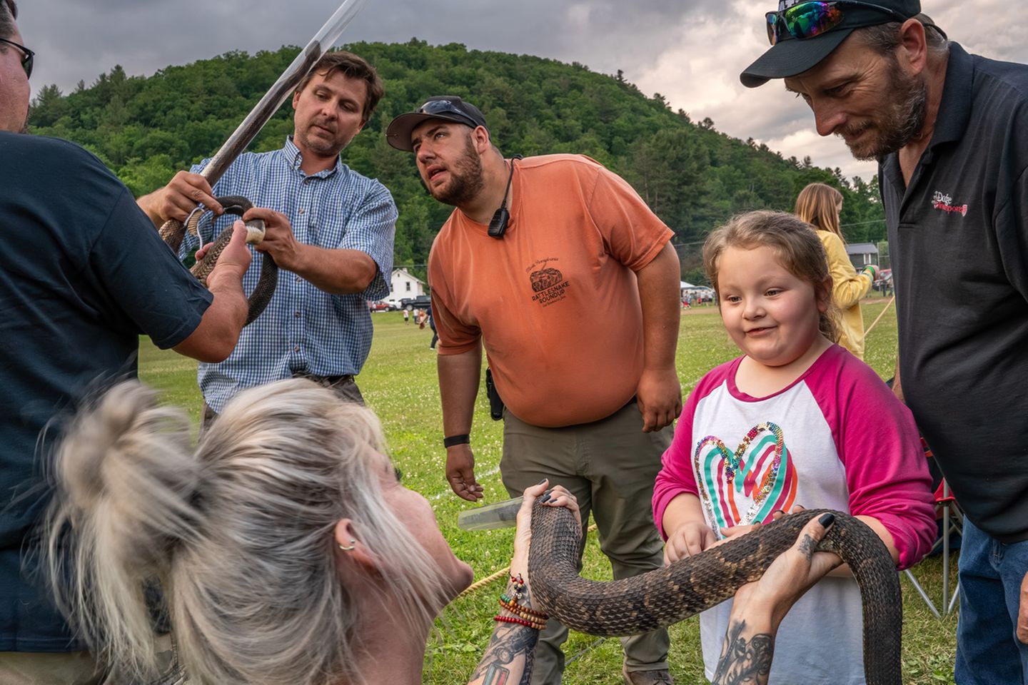 Ein Kind hält eine Klapperschlange in der Hand, um sie herum erwachsene Personen