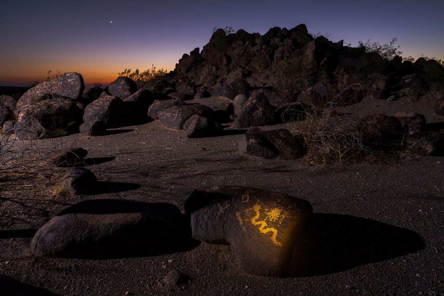 In einer Landschaft leuchtet ein mit gelber Farbe bemalter Stein auf, welcher das Symbol einer Schlange zeigt