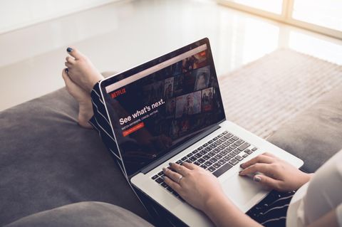 "Comfort Binge": Eine Frau sitzt auf dem Sofa und hat einen Laptop auf dem Schoß. Netflix ist geöffnet.