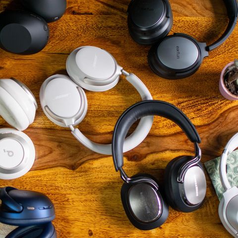 Various pairs of over-ear headphones lie on a wooden table