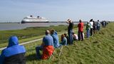 Ditzum, Niedersachsen. Das Kreuzfahrtschiff "Disney Destiny" wurde am Samstag an der Ems zur großen Deich-Attraktion. Schaulustige beobachten das neu gebaute, 340 Meter lange Schiff auf seiner Reise von der Papenburger Meyer-Werft zur Nordsee. Dabei musste der Ozeanriese eine 40 Kilometer lange Emspassage meistern – gezogen von Schleppern und mit dem Heck voran. Das Schiff verfügt über 1250 Kabinen und bietet Platz für rund 4000 Passagiere