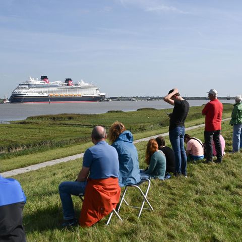 Ditzum, Niedersachsen. Das Kreuzfahrtschiff "Disney Destiny" wurde am Samstag an der Ems zur großen Deich-Attraktion. Schaulustige beobachten das neu gebaute, 340 Meter lange Schiff auf seiner Reise von der Papenburger Meyer-Werft zur Nordsee. Dabei musste der Ozeanriese eine 40 Kilometer lange Emspassage meistern – gezogen von Schleppern und mit dem Heck voran. Das Schiff verfügt über 1250 Kabinen und bietet Platz für rund 4000 Passagiere