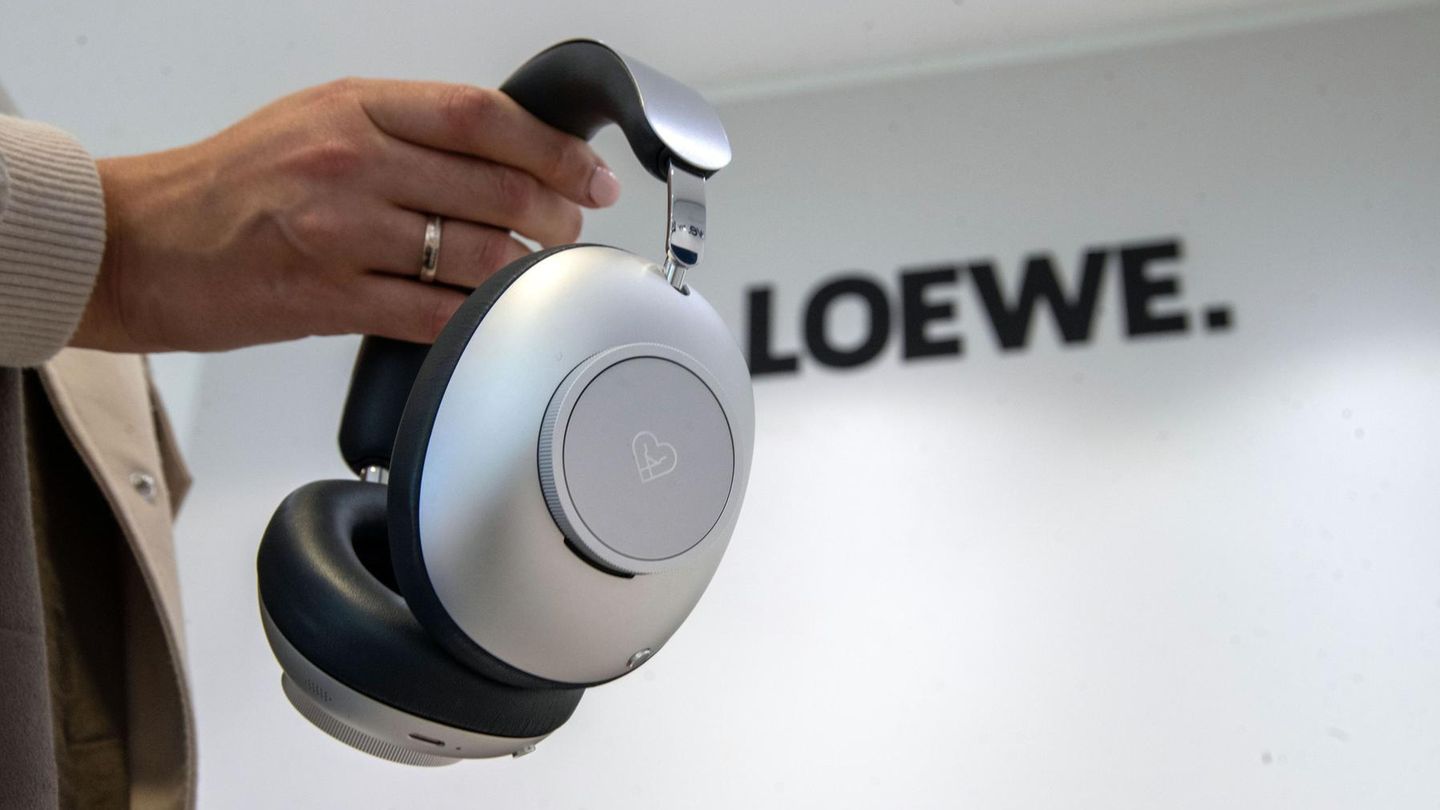 Eine Frau hält einen Kopfhörer in der Hand. An der Wand dahinter ist der Schriftzug "Loewe" zu lesen