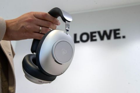 Eine Frau hält einen Kopfhörer in der Hand. An der Wand dahinter ist der Schriftzug "Loewe" zu lesen