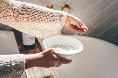 Frau streut Badesalz in die Badewanne