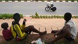 Kigali, Ruanda. Zwei Jungs werden bei ihrem Kartenspiel von der Rennradfahrerin Felicity Wilson-Haffenden aus Australien unterbrochen. Derzeit findet in der ruandischen Hauptstadt die 98. UCI Cycling World Championships statt
