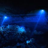 Meeresfotografie: Taucher in der Yab Yum Höhle, welche sich in der Dunkelheit mit ihren blauen Lampen von der Umgebung abheben