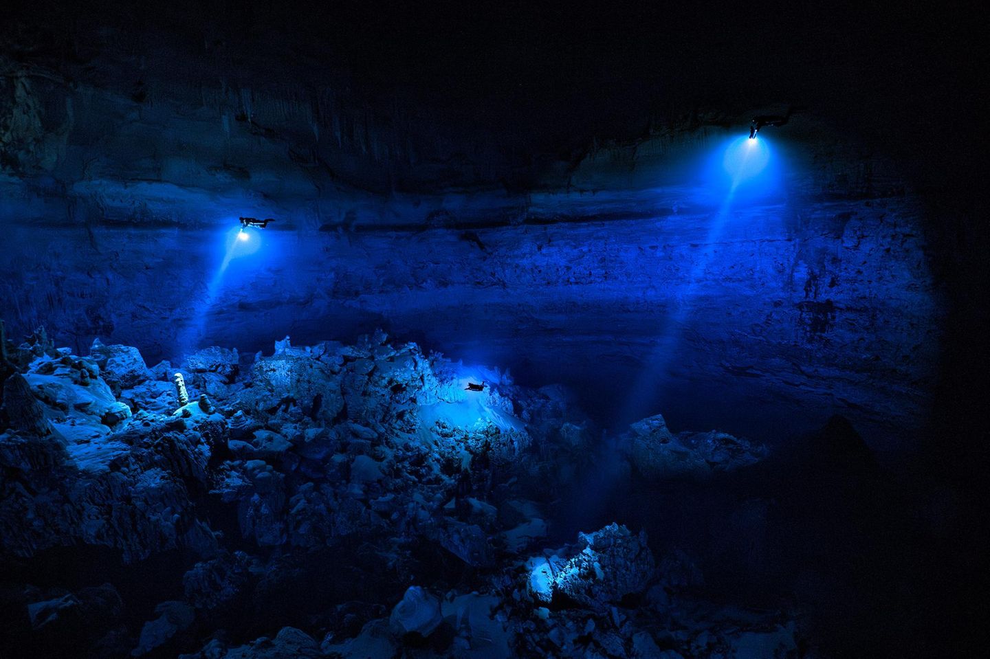 Meeresfotografie: Taucher in der Yab Yum Höhle, welche sich in der Dunkelheit mit ihren blauen Lampen von der Umgebung abheben