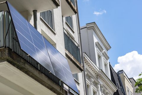 Solarpanels an Balkonen einer weißen Hausfassade, im Hintergrund ist blauer Himmel zu sehen