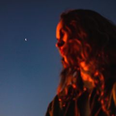 Menstruation und Mond: Eine Frau wird nachts in Rot angeblitzt, im Hintergrund sieht man den Mond
