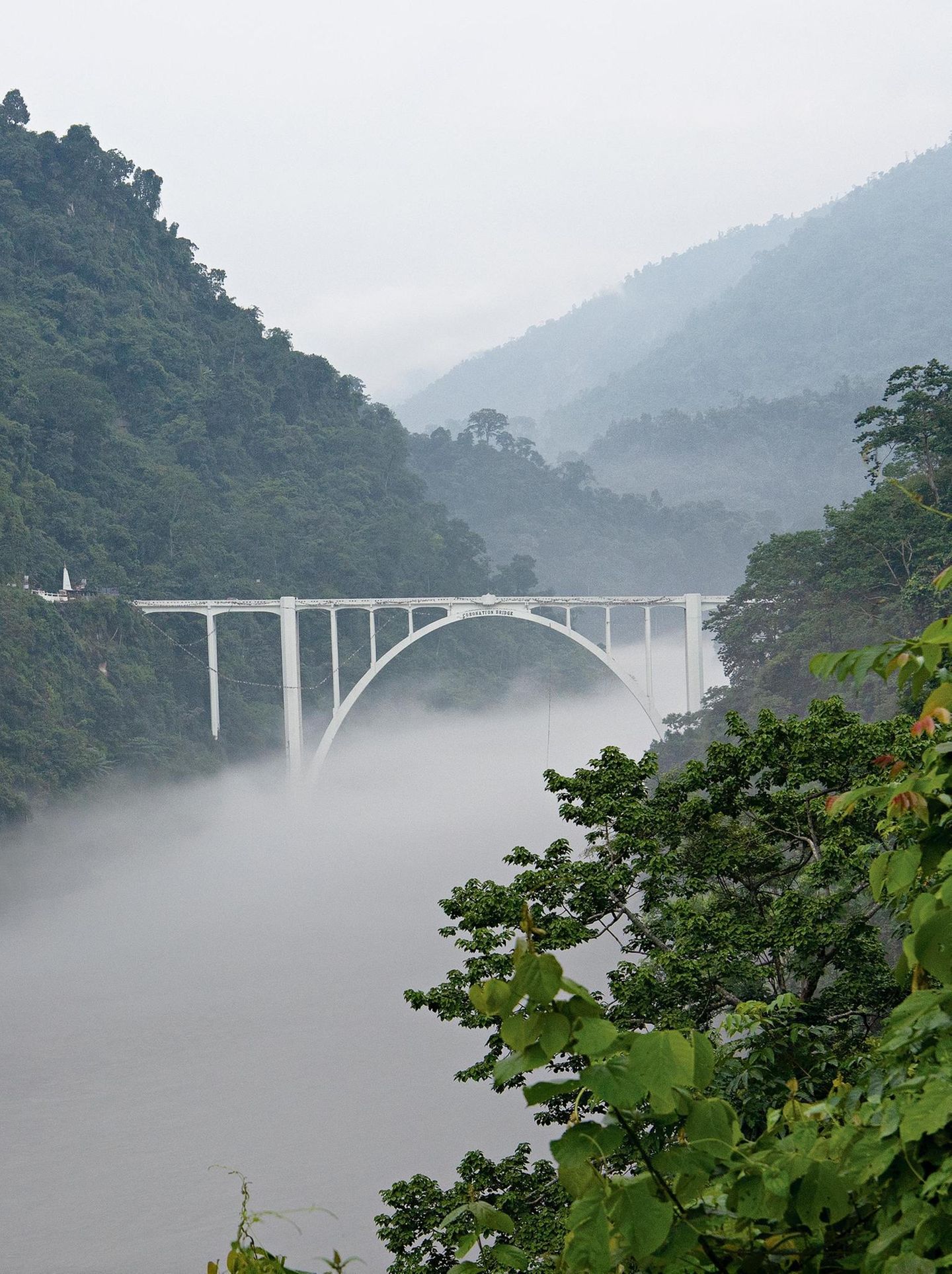 Brücke über einen Fluss, im Tal liegt Nebel