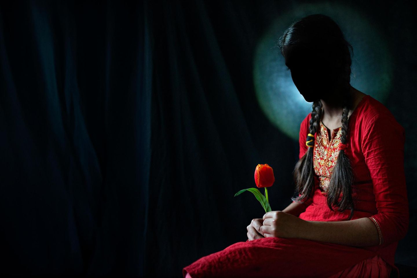Junge Frau in einem roten Kleid, ihr Gesicht ist im Schatten. Sie hält eine rote Tulpe