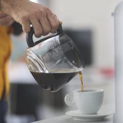 Eine Person gießt im Büro Kaffee aus einer Kanne in eine Tasse