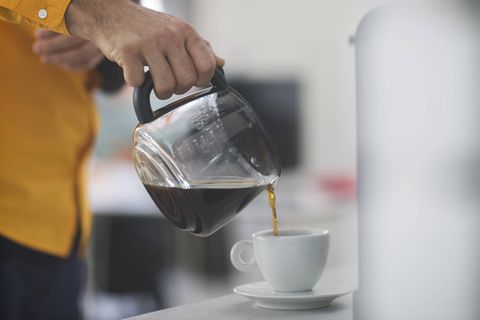 Eine Person gießt im Büro Kaffee aus einer Kanne in eine Tasse