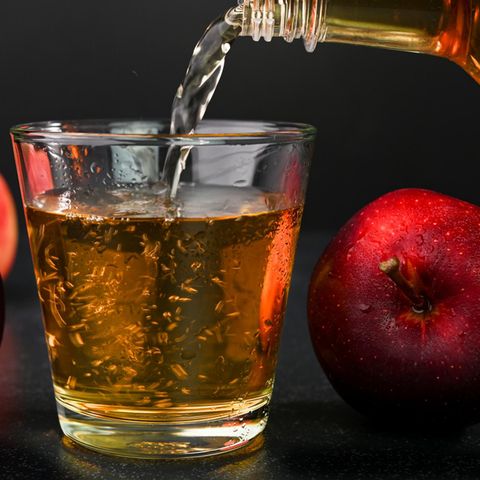 Apfelessig wird aus einer Flasche in ein Glass geschüttet