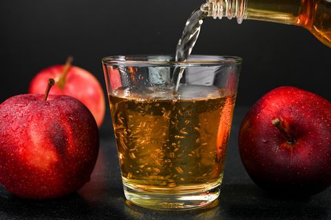 Apfelessig wird aus einer Flasche in ein Glass geschüttet
