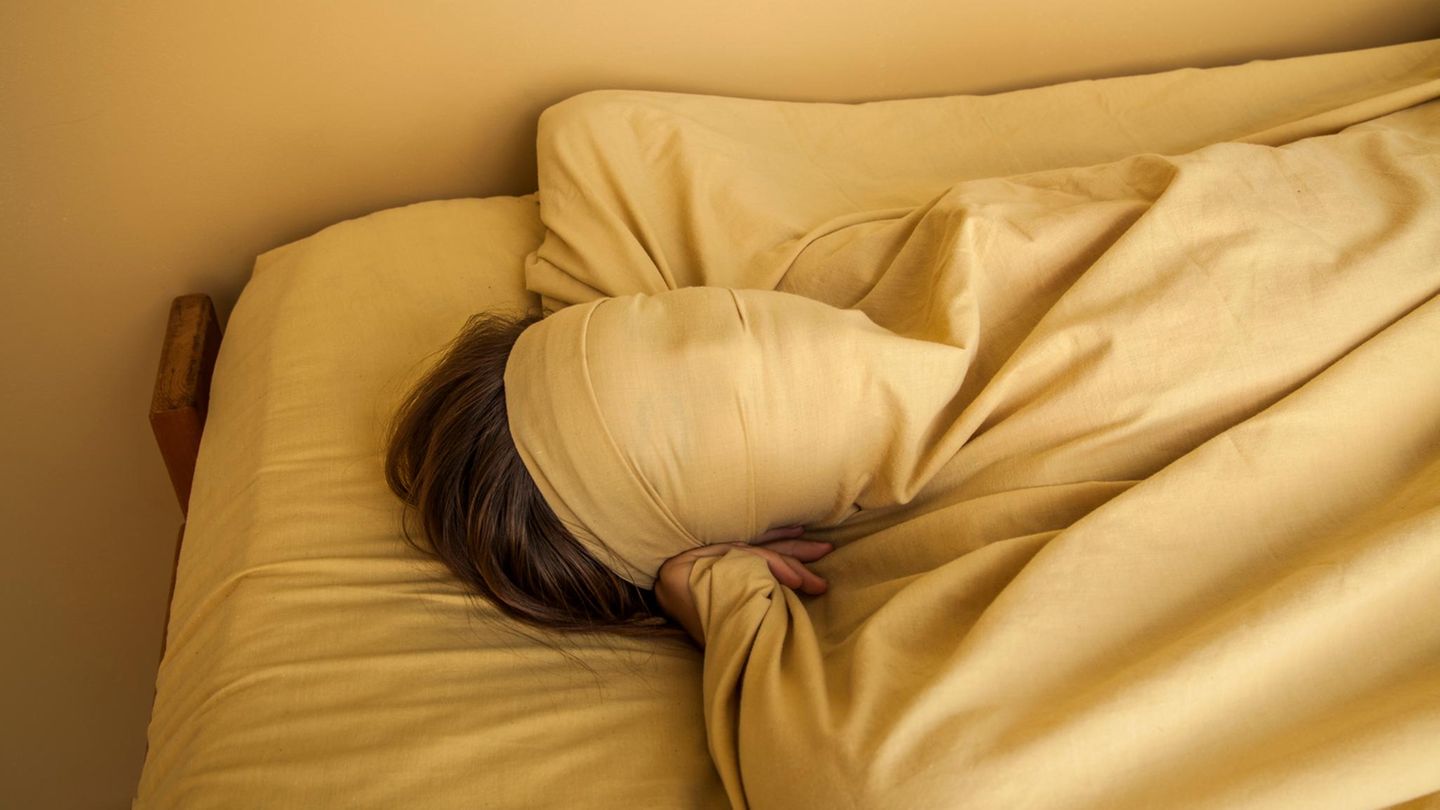 Eine Frau verhüllt mit einem Laken ihr Gesicht