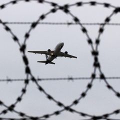 Ein Flugzeug startet - fotografiert durch Stacheldraht am Flughafenzaun