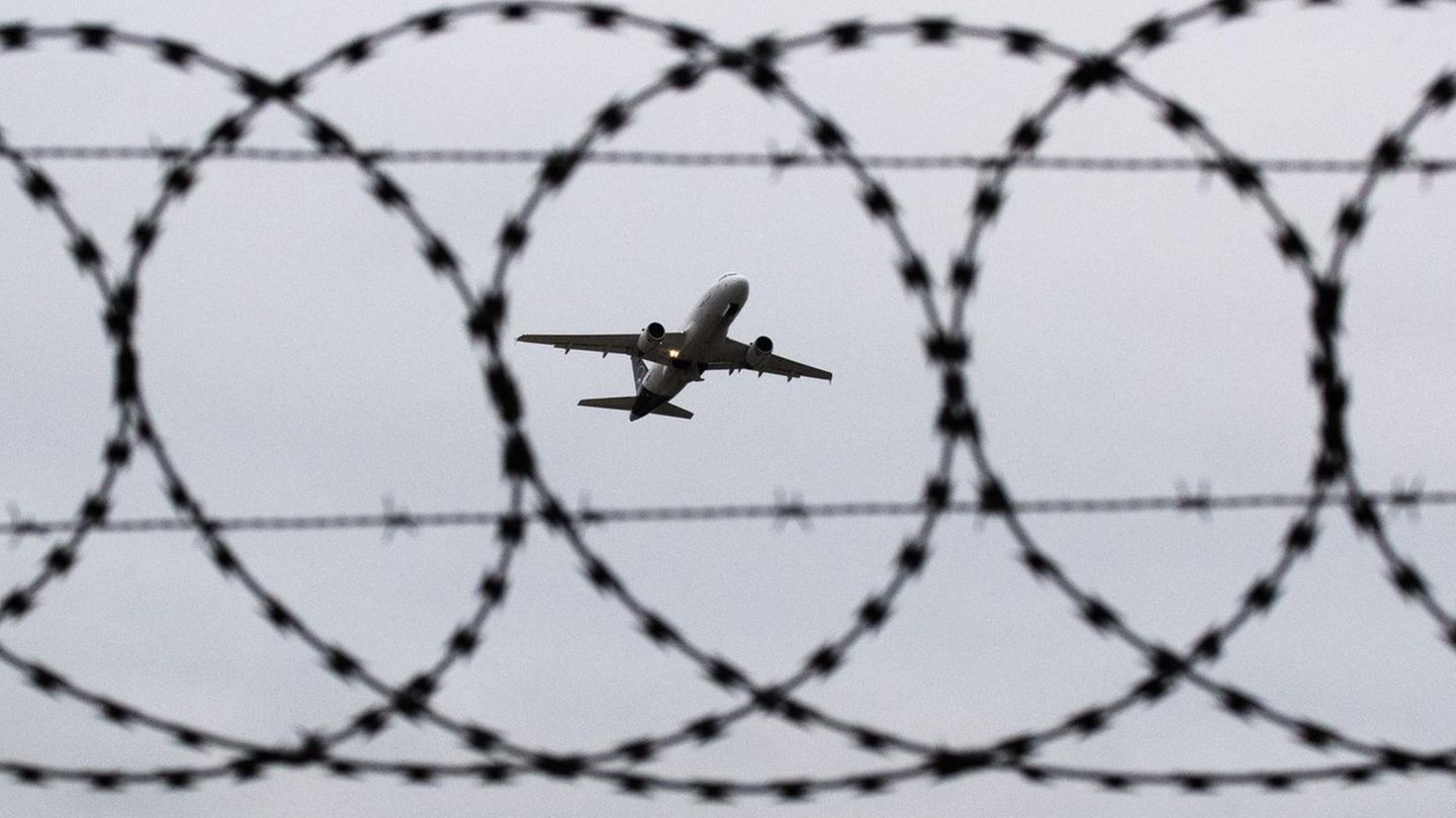 Ein Flugzeug startet - fotografiert durch Stacheldraht am Flughafenzaun