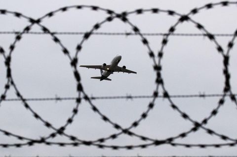 Ein Flugzeug startet - fotografiert durch Stacheldraht am Flughafenzaun
